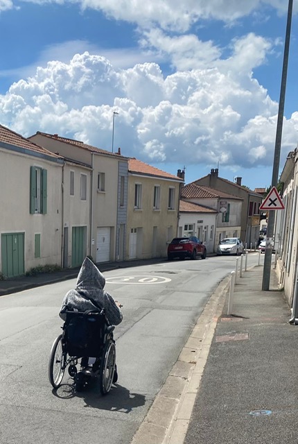 Personne en fauteuil roulant circulant sur la chaussée de la rue Marius-Lacroix faute de trottoir praticable