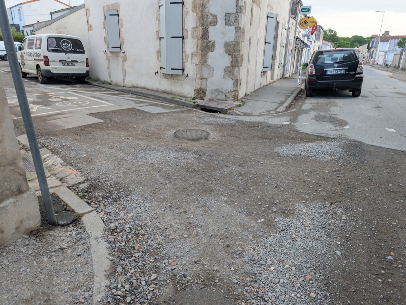 Rue Marius-Lacroix le 30 avril 2026 : carrefour avec asphalte arraché, gravillons épars, plaque d'égout au milieu