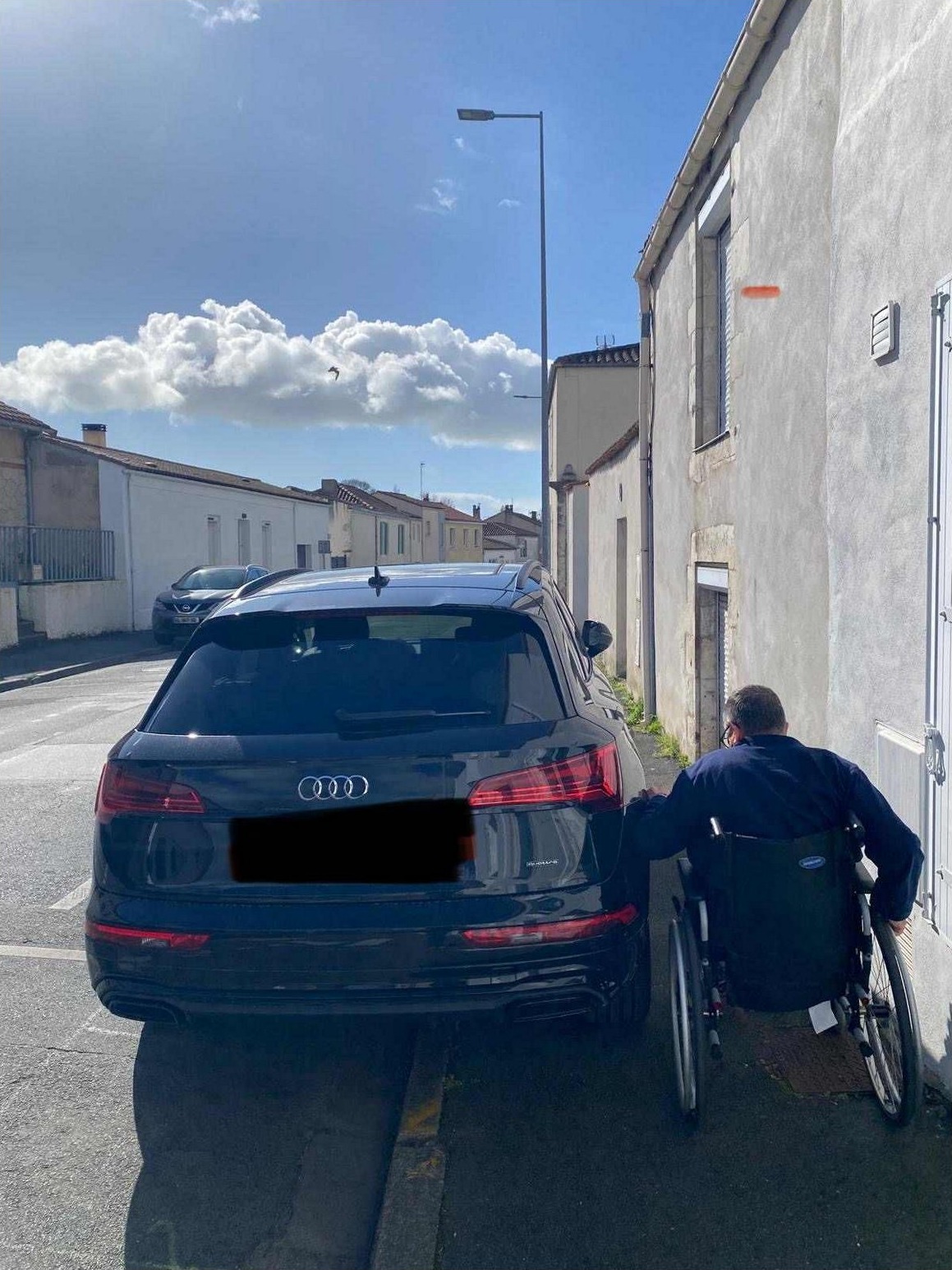 Personne en fauteuil roulant tentant de passer entre une voiture stationnée et un mur