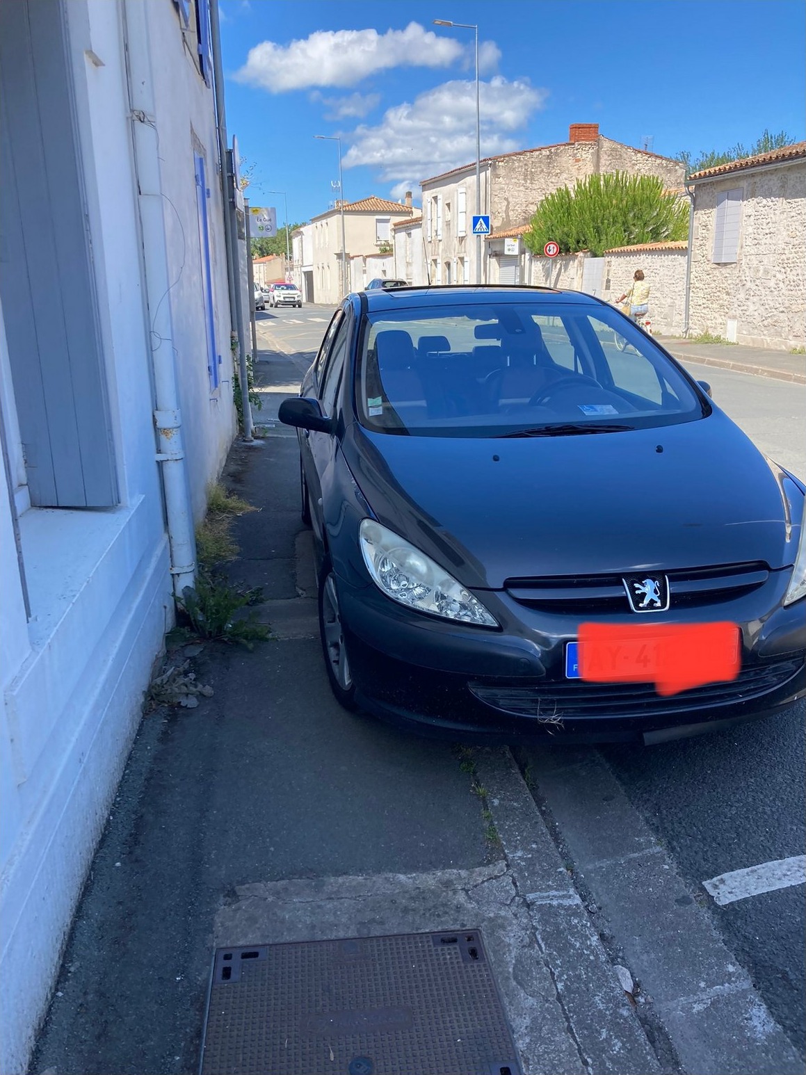 Voiture stationnée sur le trottoir devant un domicile, place PMR signalée mais inaccessible
